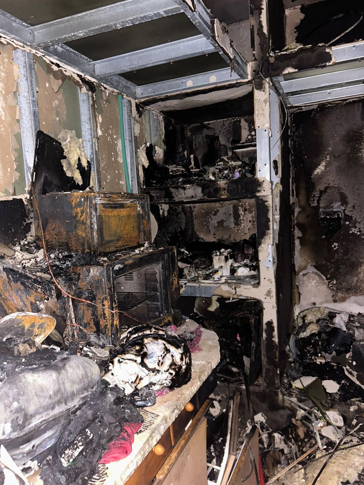 A kitchen corner burned to the core — a charred oven and microwave